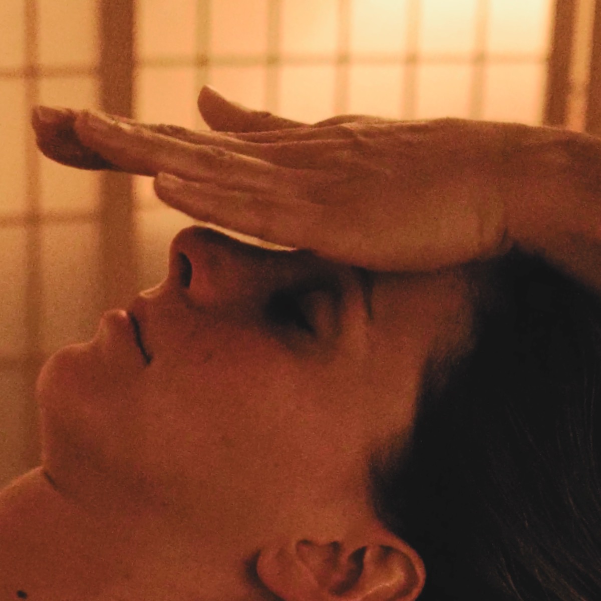 Close-up of a client fully relaxed during a facial lymphatic drainage session, eyes closed, hand resting over the forehead